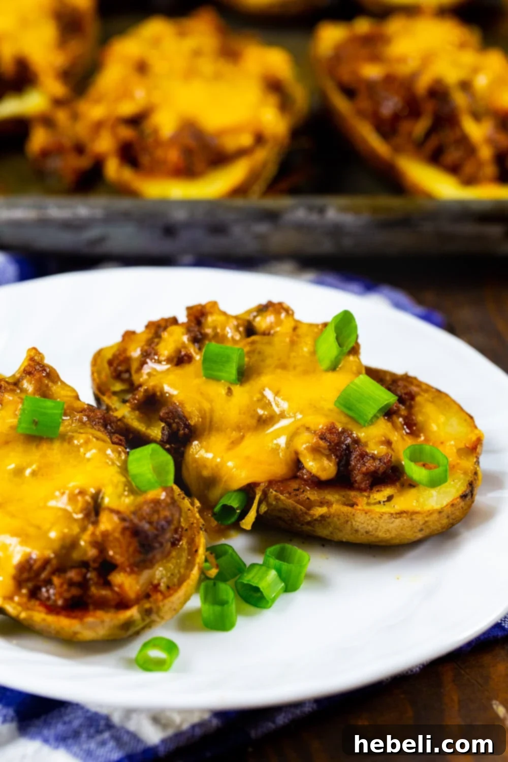Two perfectly golden and cheesy Sloppy Joe Potato Skins, garnished with fresh green onions, served on a white plate, ready to be enjoyed.