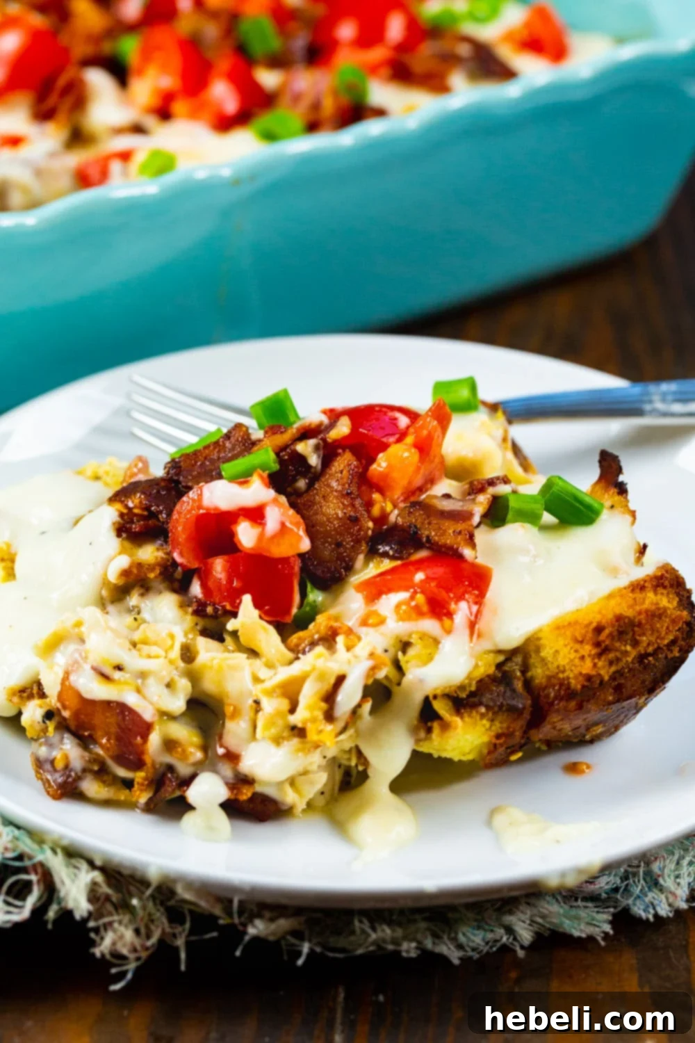 A perfect slice of Hot Brown Casserole on a white plate, showcasing its layers of turkey, bread, and cheese with sauce.