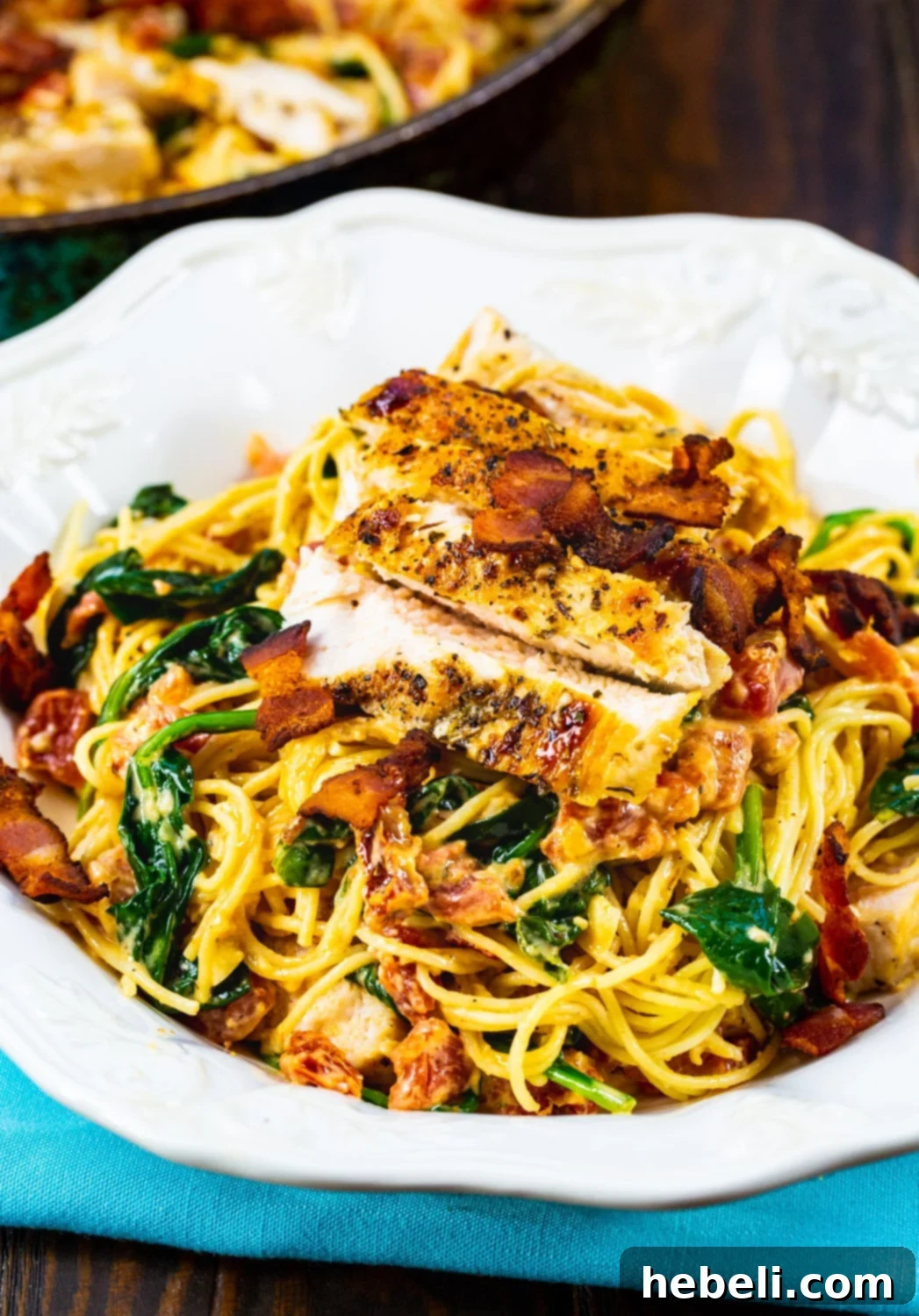 Creamy Tuscan Chicken Pasta 4 A close-up of a serving of Tuscan Chicken Pasta in a bowl, showing the creamy sauce, chicken, bacon, and spinach.