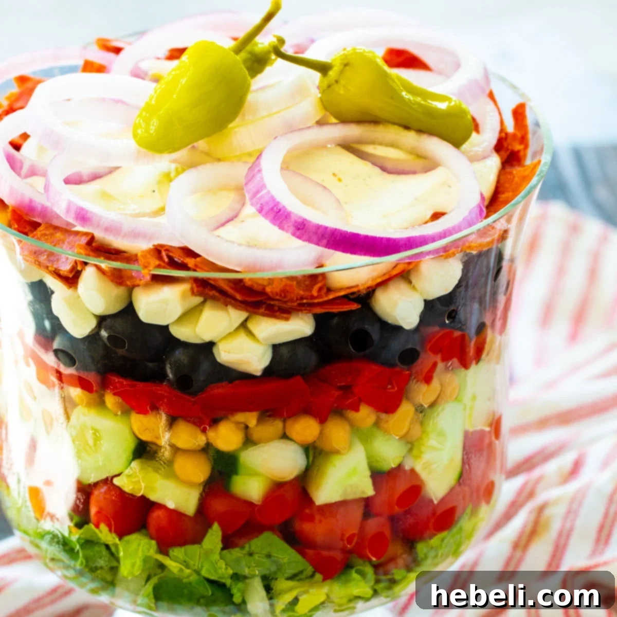A stunning Italian Layered Salad, meticulously arranged in a clear trifle bowl, showcasing distinct layers of fresh ingredients.