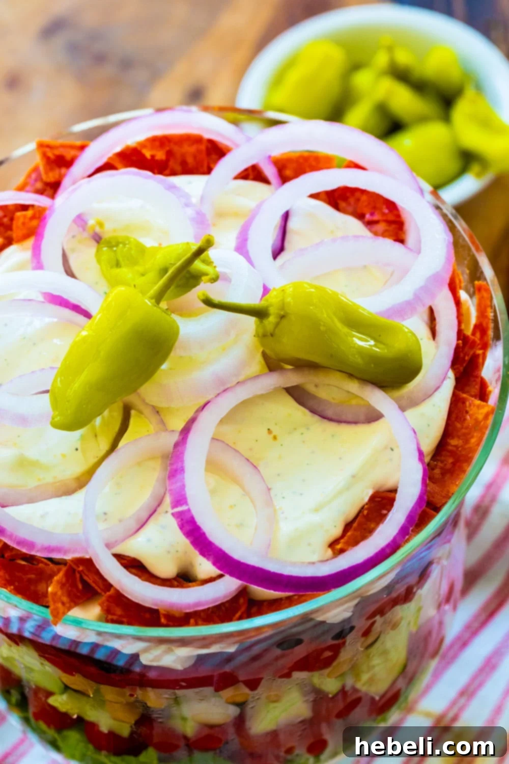 The top view of the vibrant Italian Layered Salad, adorned with bright pepperoncini peppers and red onion slices.