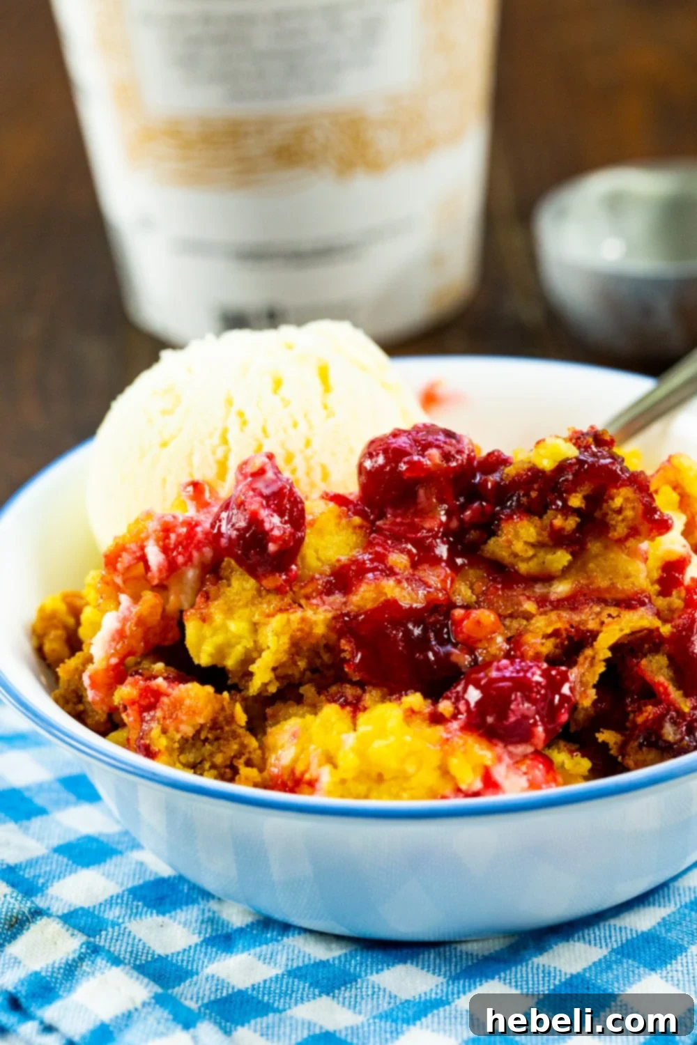 Crock Pot Cherries and Cream Dump Cake topped with a scoop of vanilla ice cream in a white bowl.
