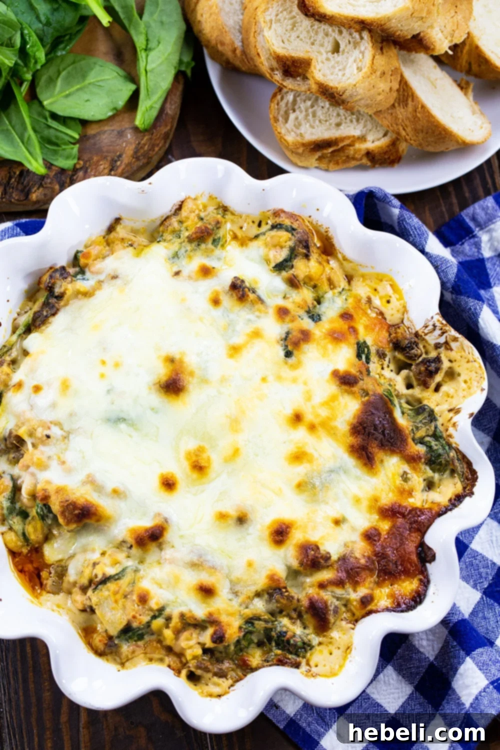 An inviting overhead shot of the Tuscan Sausage and White Bean Dip in a white ceramic pie plate, presented with a platter of golden, toasted baguette slices on the side.