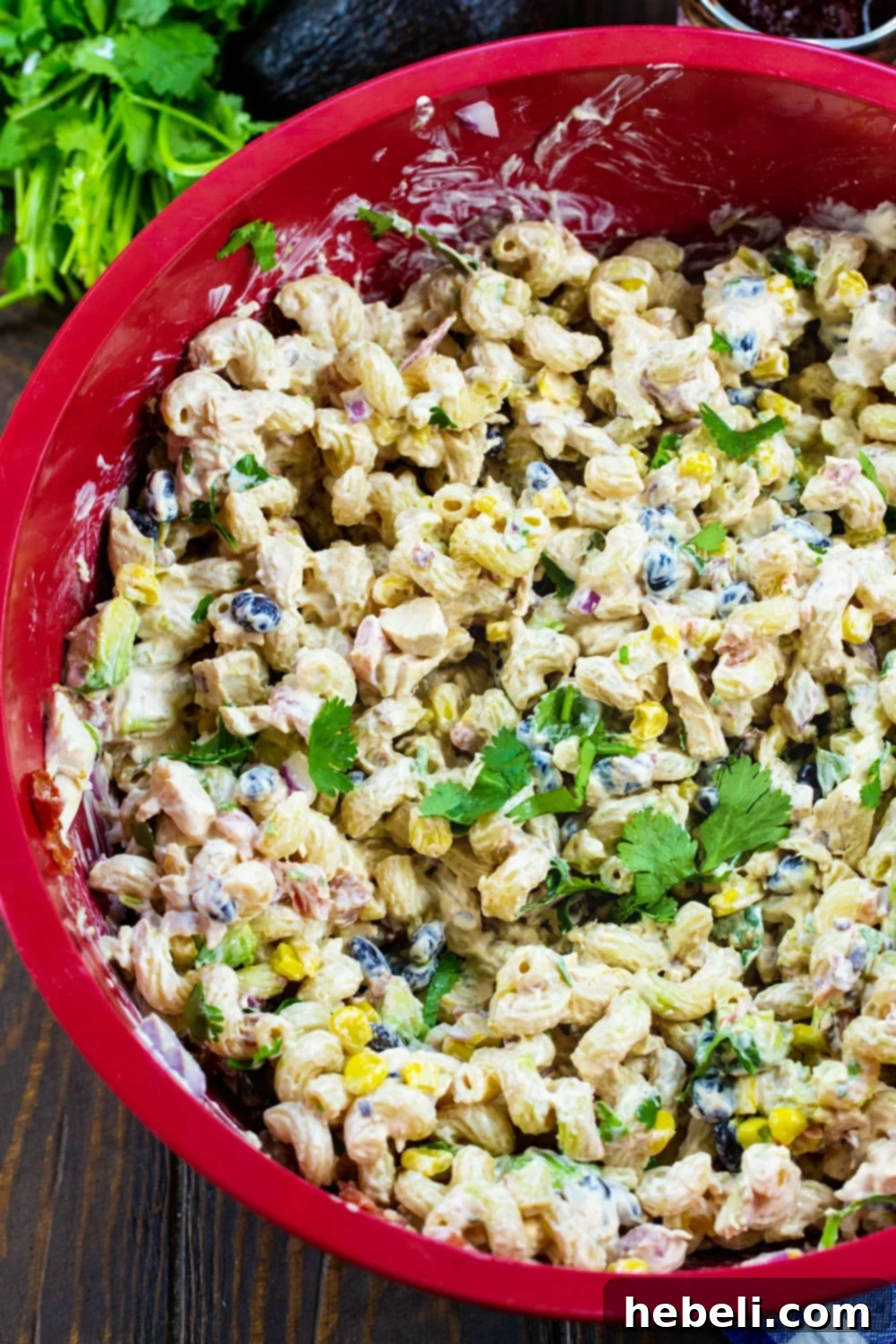 Creamy Chipotle Chicken Pasta Salad 3 Close-up shot of pasta salad being mixed in a large red bowl, showcasing fresh ingredients.