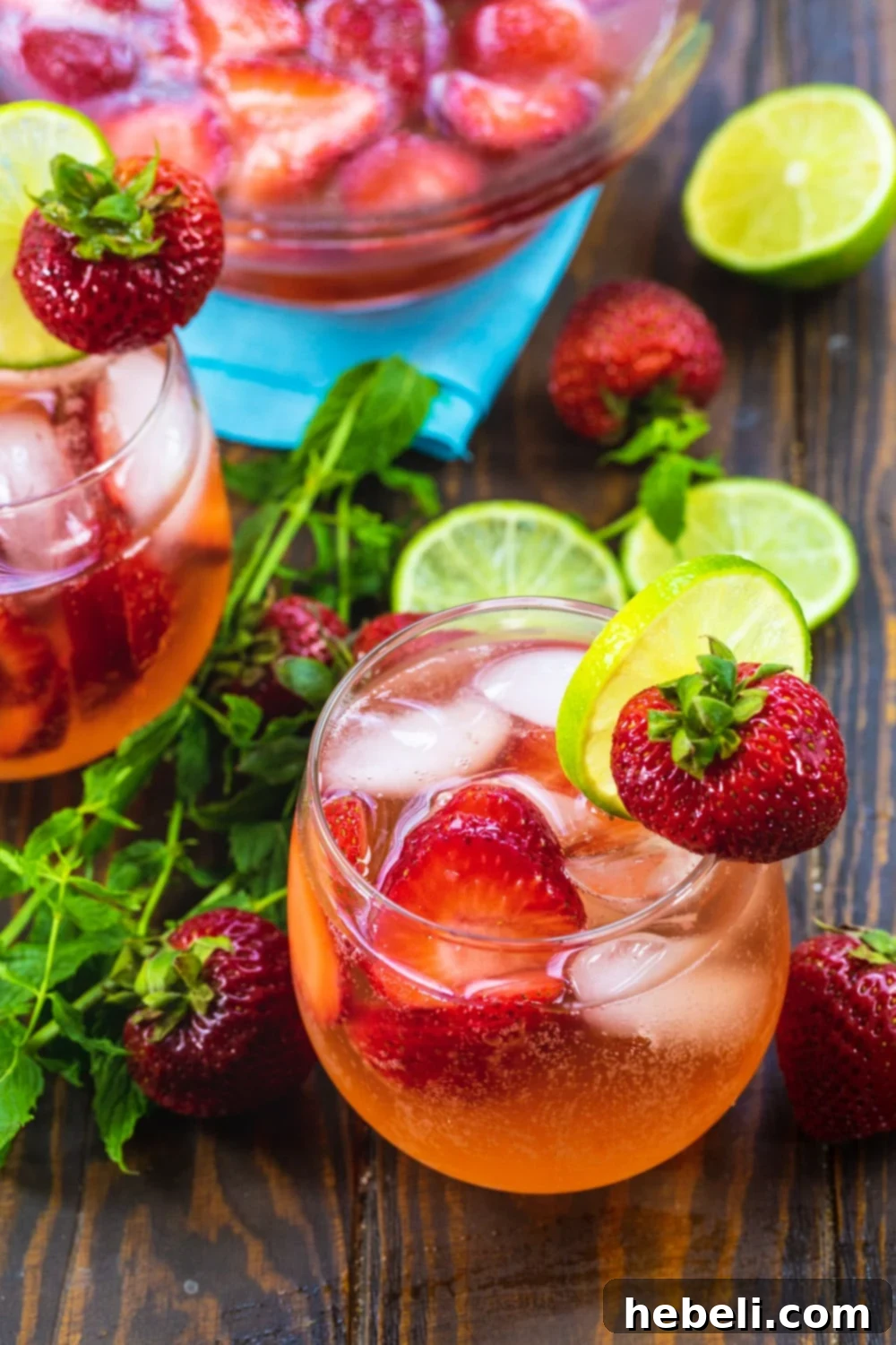 Two glasses of Strawberry Shortcake Sangria, with a full pitcher in the background, adorned with fresh fruit.