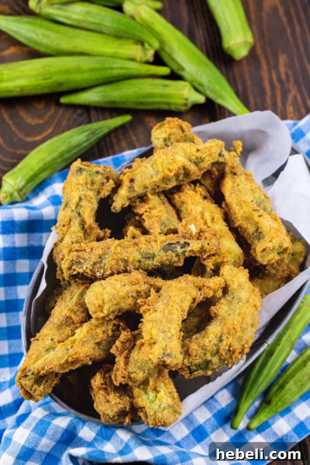 Whole Fried Okra with fresh okra pods surrounding it on a wooden surface.