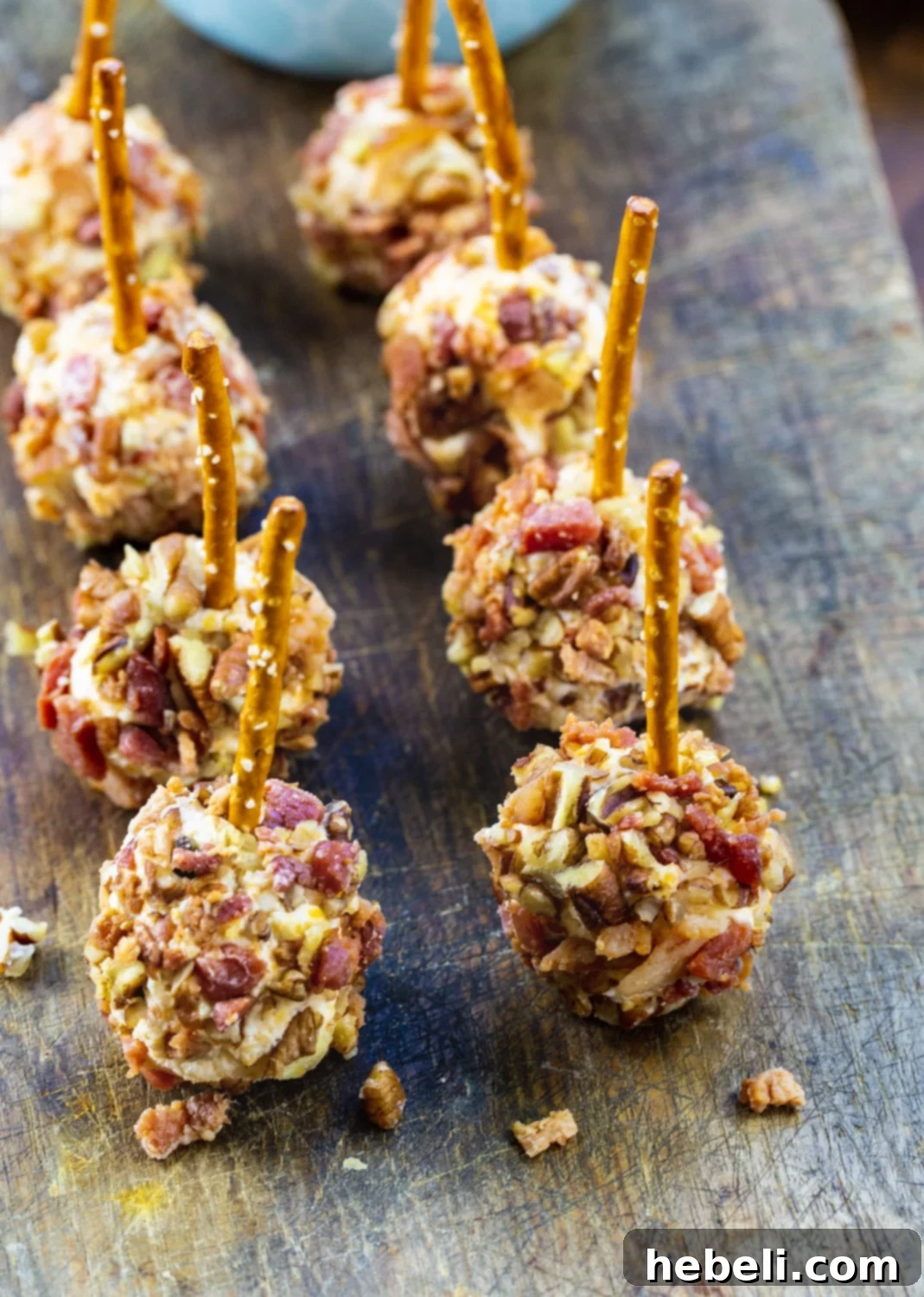 Bacon Cheese Ball Delights 3 Bacon and Pecan coated Mini Cheese Balls on a wooden cutting board, garnished with fresh herbs.