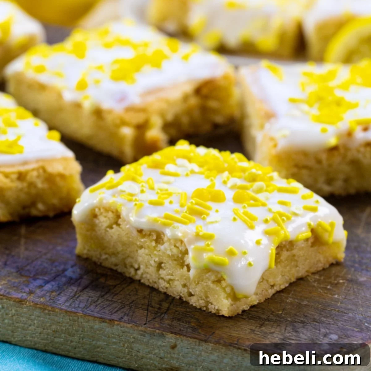 Lemon Cookie Bars topped with yellow sprinkles on a wood cutting board.