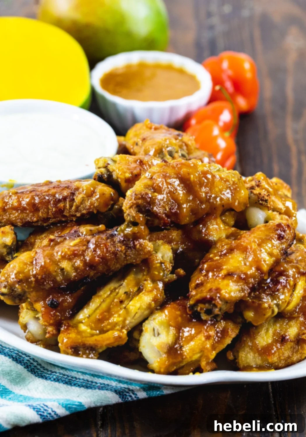 Sweet Heat Mango Habanero Wings 4 A close-up shot of Mango Habanero Chicken Wings on a plate, with fresh mango slices and vibrant habanero peppers blurred in the background, highlighting the key ingredients.