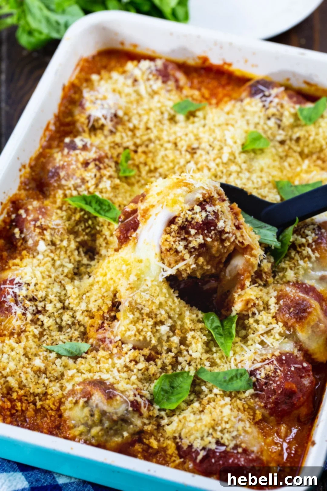 Baked Chicken Parmesan Meatballs simmering in tomato sauce, covered with melted cheese in a ceramic baking dish.