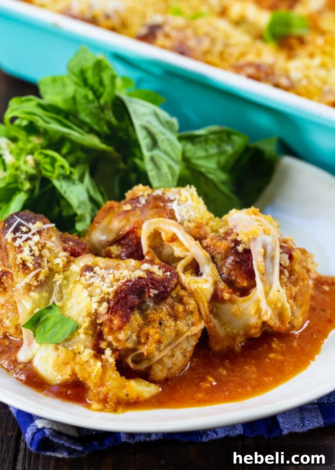 Three Chicken Parmesan Meatballs on a white plate, garnished with fresh basil leaves, ready to be enjoyed.
