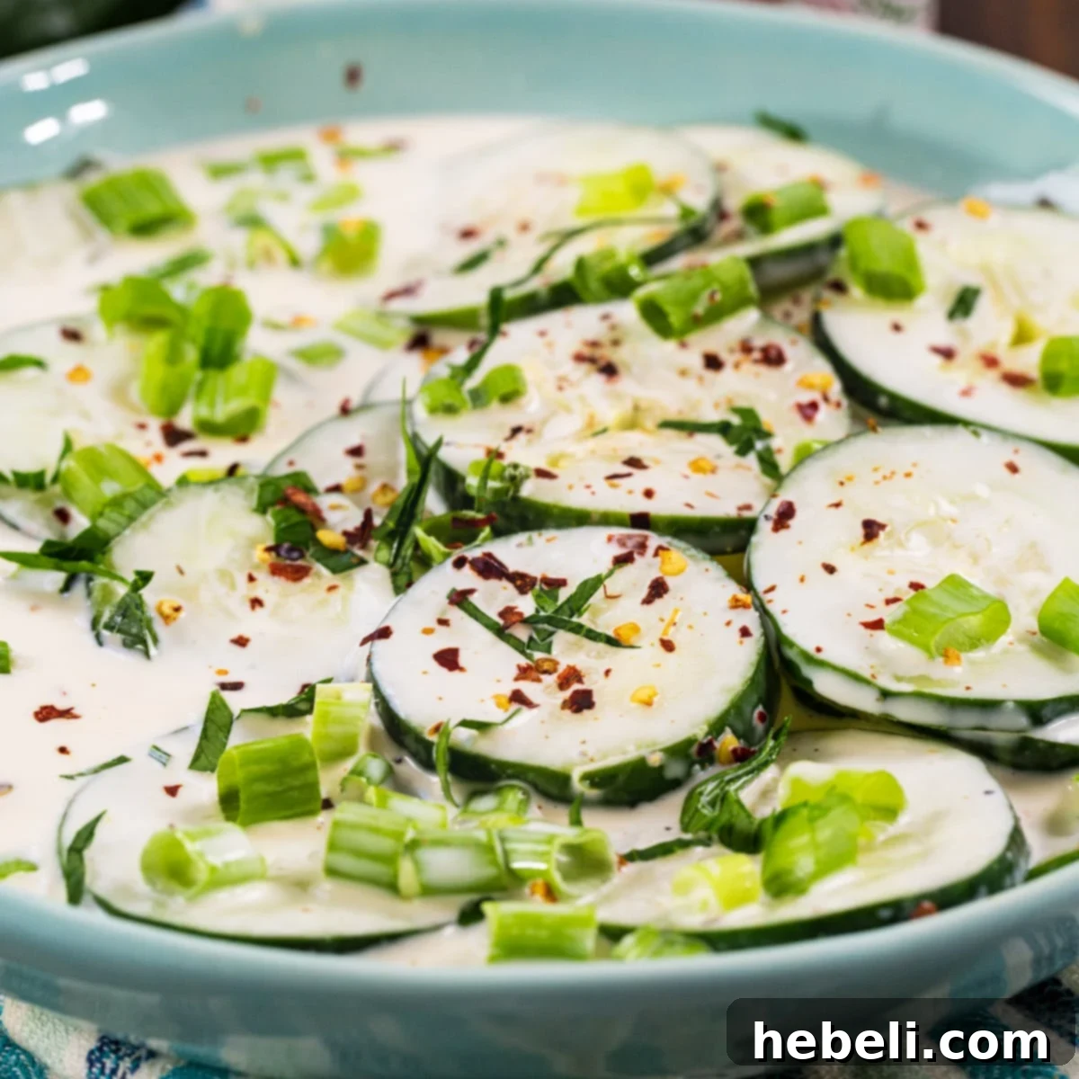Creamy Spicy Cucumbers in a beautiful blue bowl, garnished with fresh herbs, ready to be served.