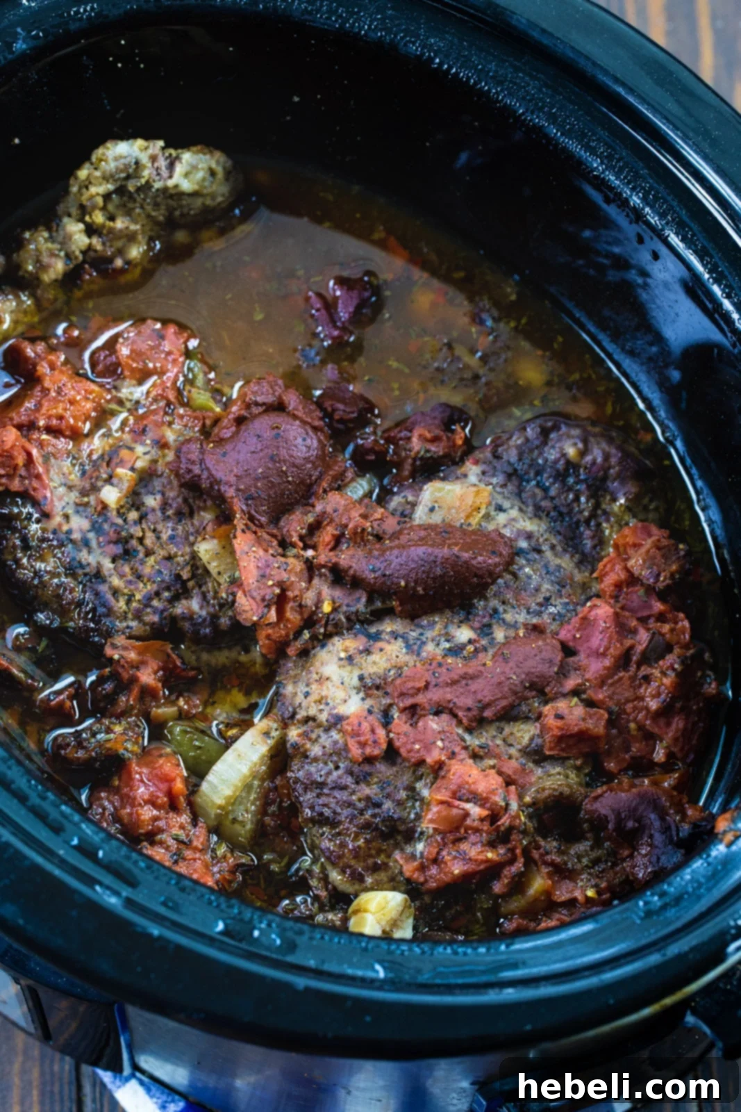 Tender Slow Cooker Swiss Steak 3 Perfectly cooked Swiss steak simmering in a rich, red tomato sauce inside a slow cooker, ready to be served.