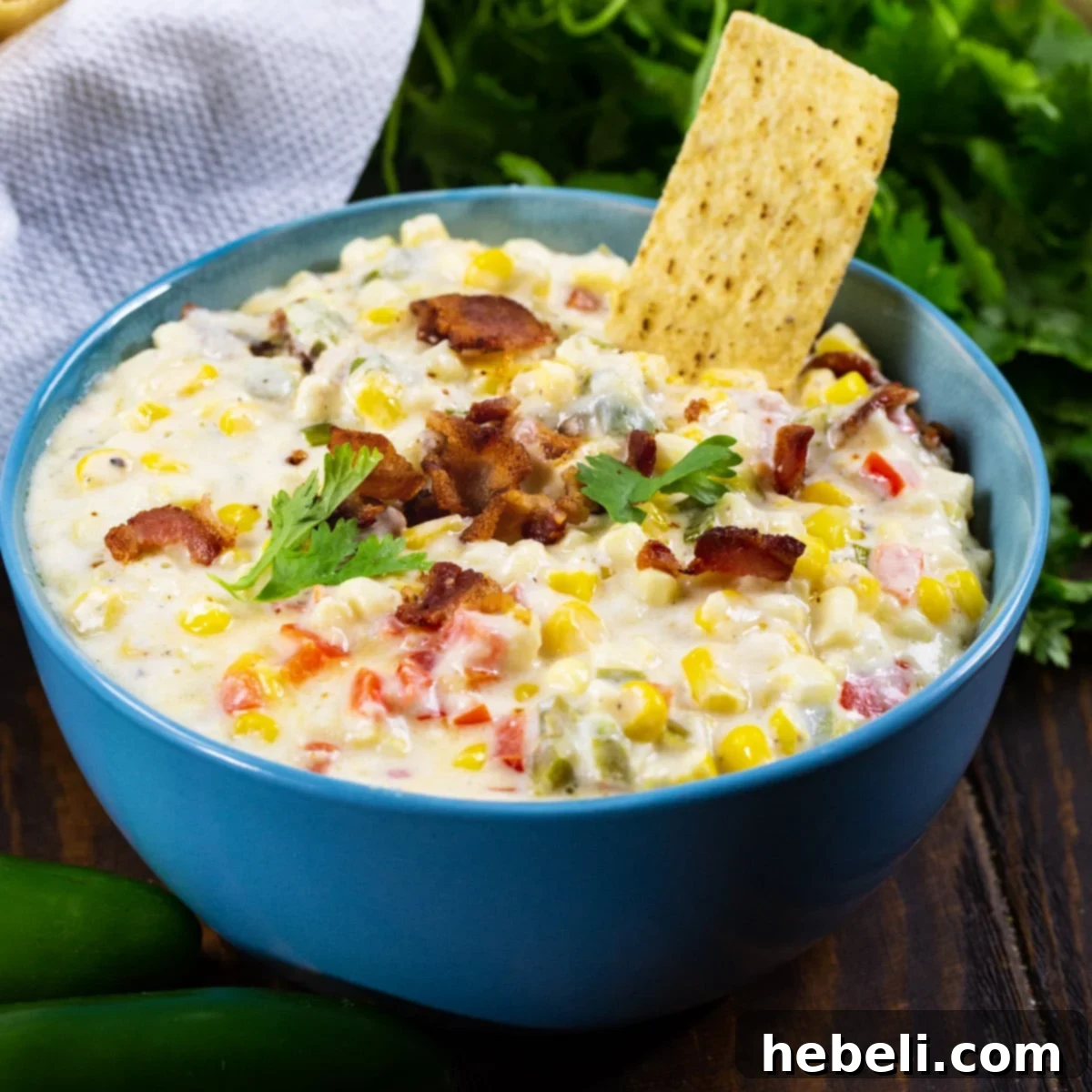 Zesty Cheesy Slow Cooker Corn Dip 2 A vibrant blue bowl filled with creamy Slow Cooker Jalapeno Popper Corn Dip, generously garnished with fresh cilantro and crispy bacon bits, ready to be served with a side of golden tortilla chips.