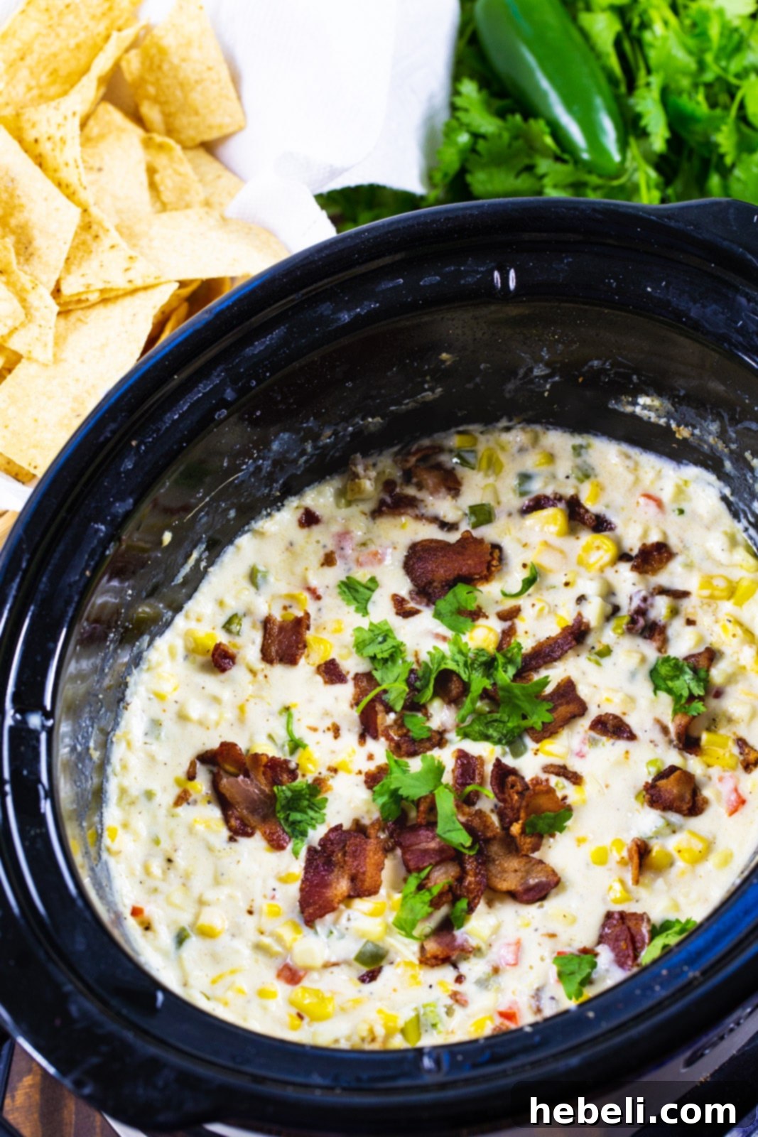 Zesty Cheesy Slow Cooker Corn Dip 3 A black slow cooker brimming with rich, cheesy Jalapeno Popper Corn Dip, generously topped with crispy bacon bits, showcasing its warm and inviting texture.