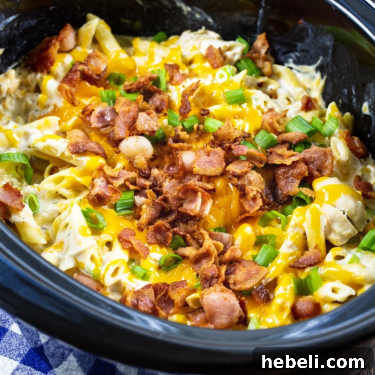 Addictive Slow Cooker Chicken Pasta 2 A vibrant, close-up shot of Slow Cooker Crack Chicken Pasta served in a crock pot, topped with melted cheese and fresh green onions.