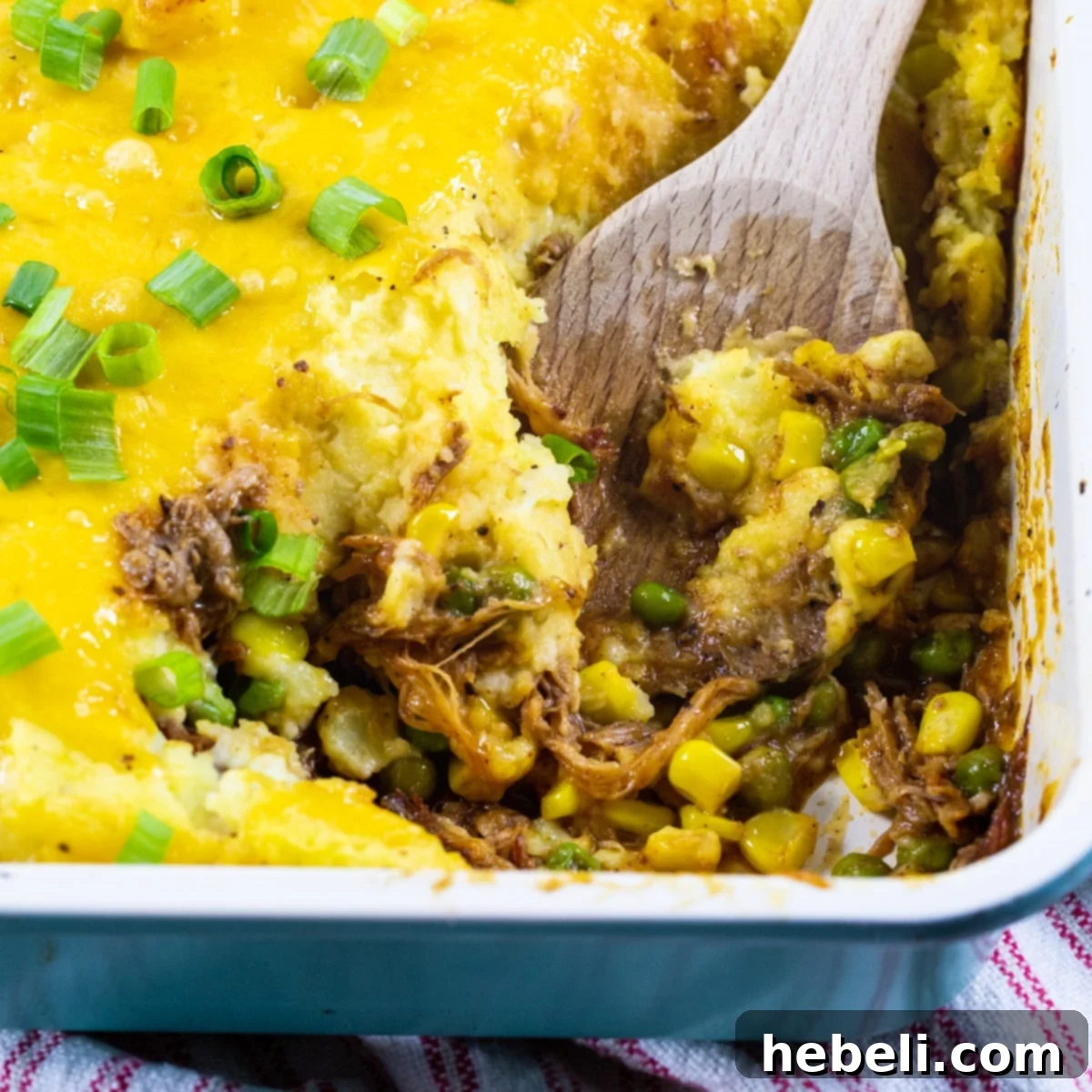 Hearty Pulled Pork Shepherds Pie 2 A rustic wooden spoon gently scooping a generous portion of Pulled Pork Shepherd's Pie from a baking dish, revealing layers of tender pork, vibrant vegetables, and creamy mashed potatoes.