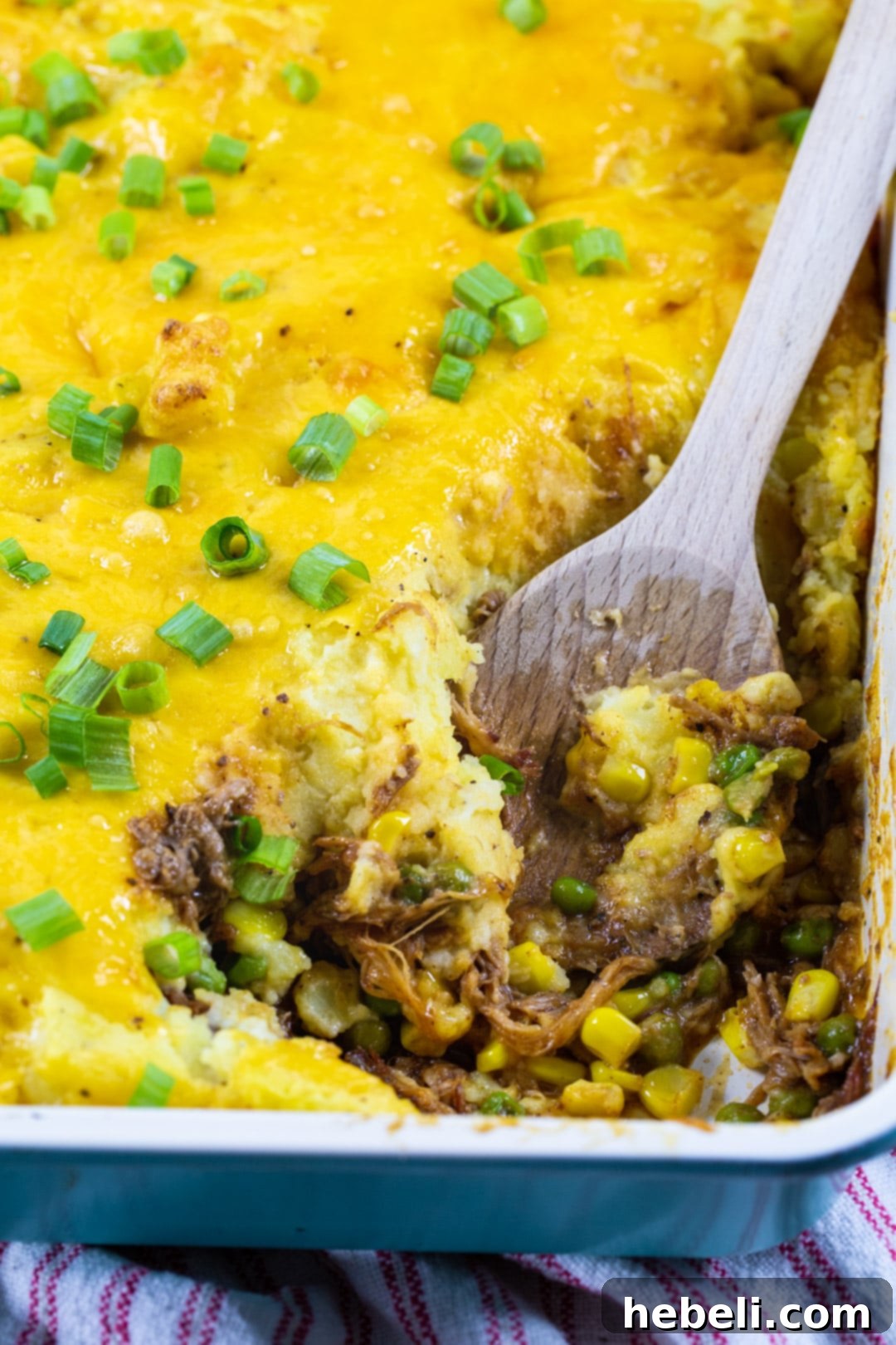 Hearty Pulled Pork Shepherds Pie 3 A serving of Pulled Pork Shepherd's Pie on a white plate, showcasing the distinct layers of mashed potatoes, vegetables, and pulled pork, with a fork poised to take a bite.