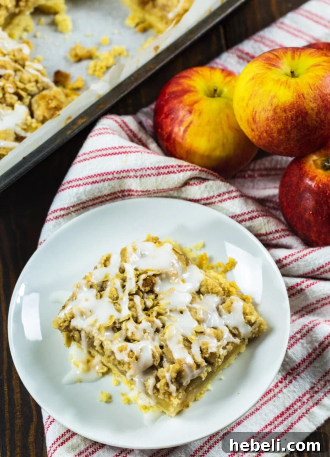 A perfectly portioned Oatmeal Crumb Apple Bar next to a scattering of fresh, crisp apples, highlighting the natural ingredients.