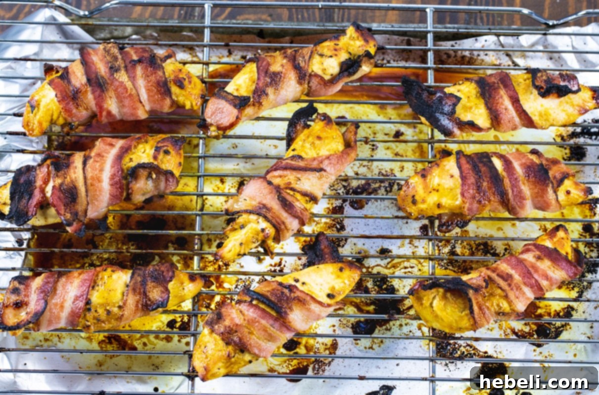 Crispy Bacon-Wrapped Honey Mustard Chicken 3 Raw chicken tenderloins precisely wrapped with slices of regular bacon, arranged neatly on a wire rack over a baking sheet, ready for the oven.