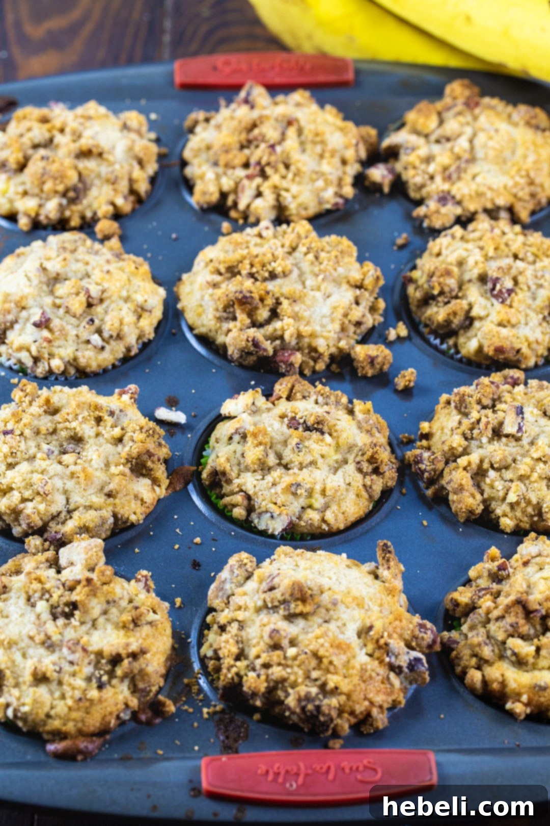 Freshly baked Bananas Foster Muffins cooling in a muffin tin, showcasing their golden-brown streusel topping.
