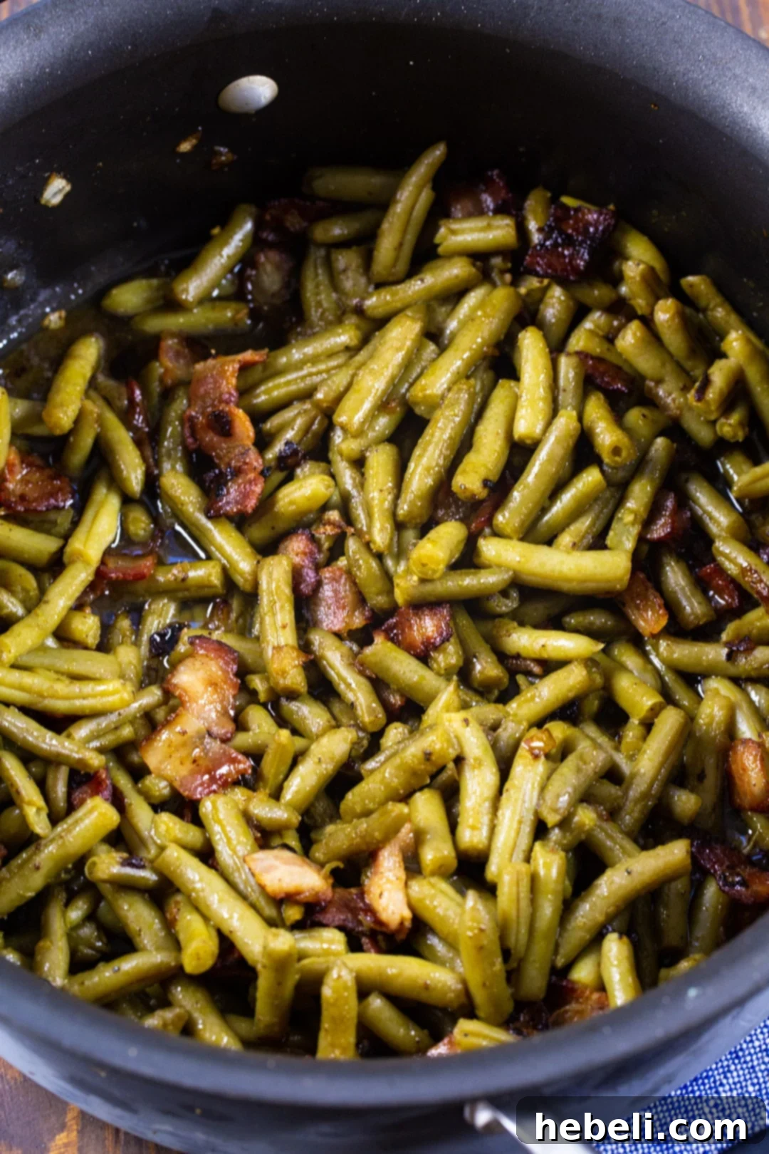 Cooked green beans simmering in a large pot with bacon and sauce.