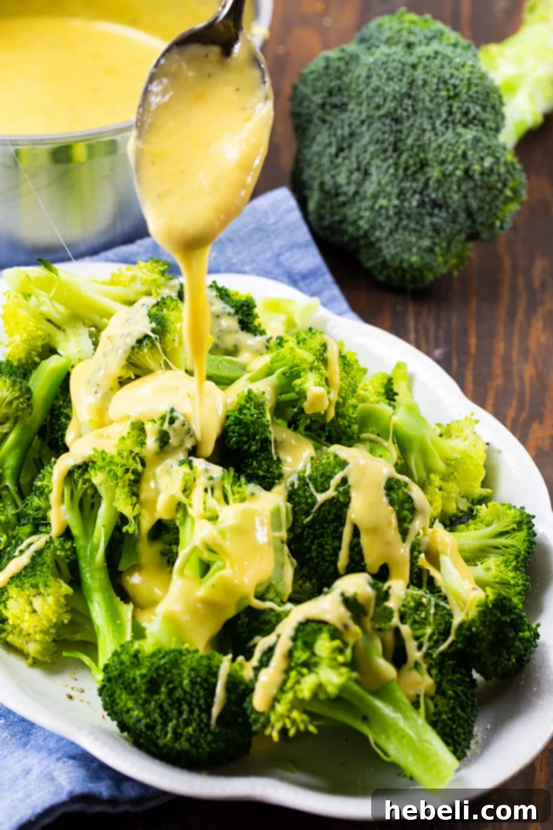 Thick, golden cheddar cheese sauce cascading beautifully over a fresh cluster of steamed broccoli.