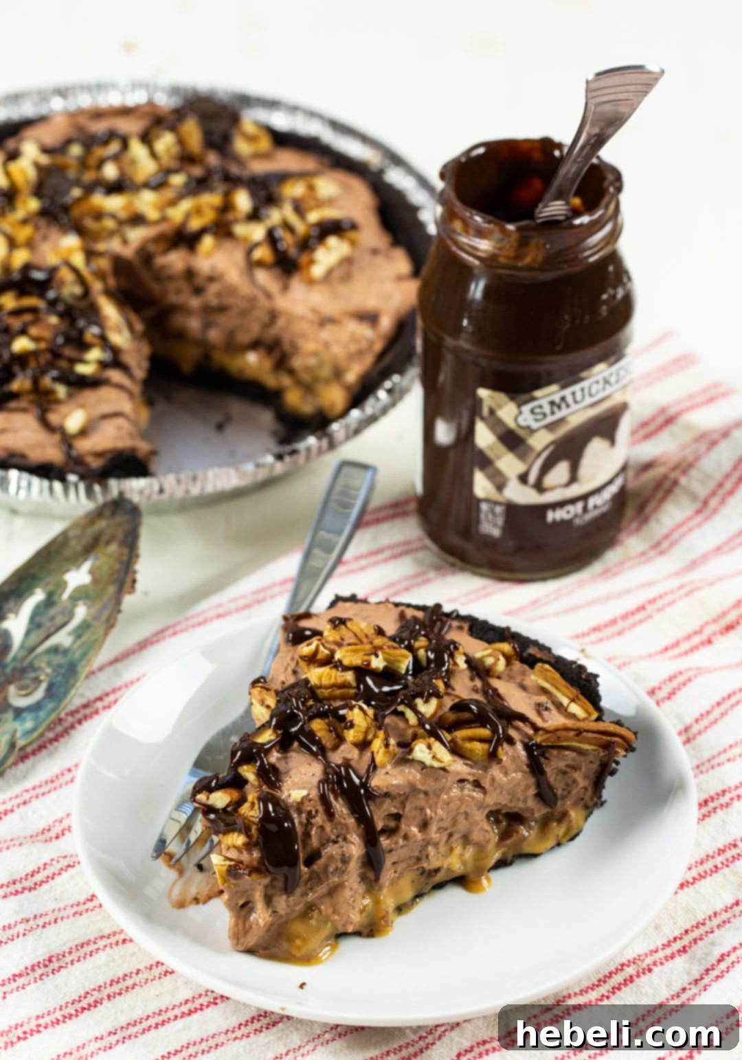 Decadent Chocolate Caramel Dream 4 A slice of Chocolate Caramel Pie on a plate, with the rest of the pie and a jar of hot fudge sauce in the softly blurred background.