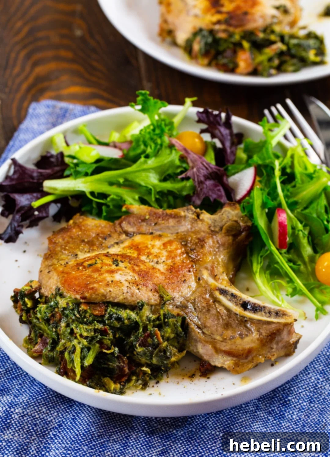 A single Spinach and Bacon Stuffed Pork Chop served on a plate with a fresh green salad, highlighting its appealing presentation.