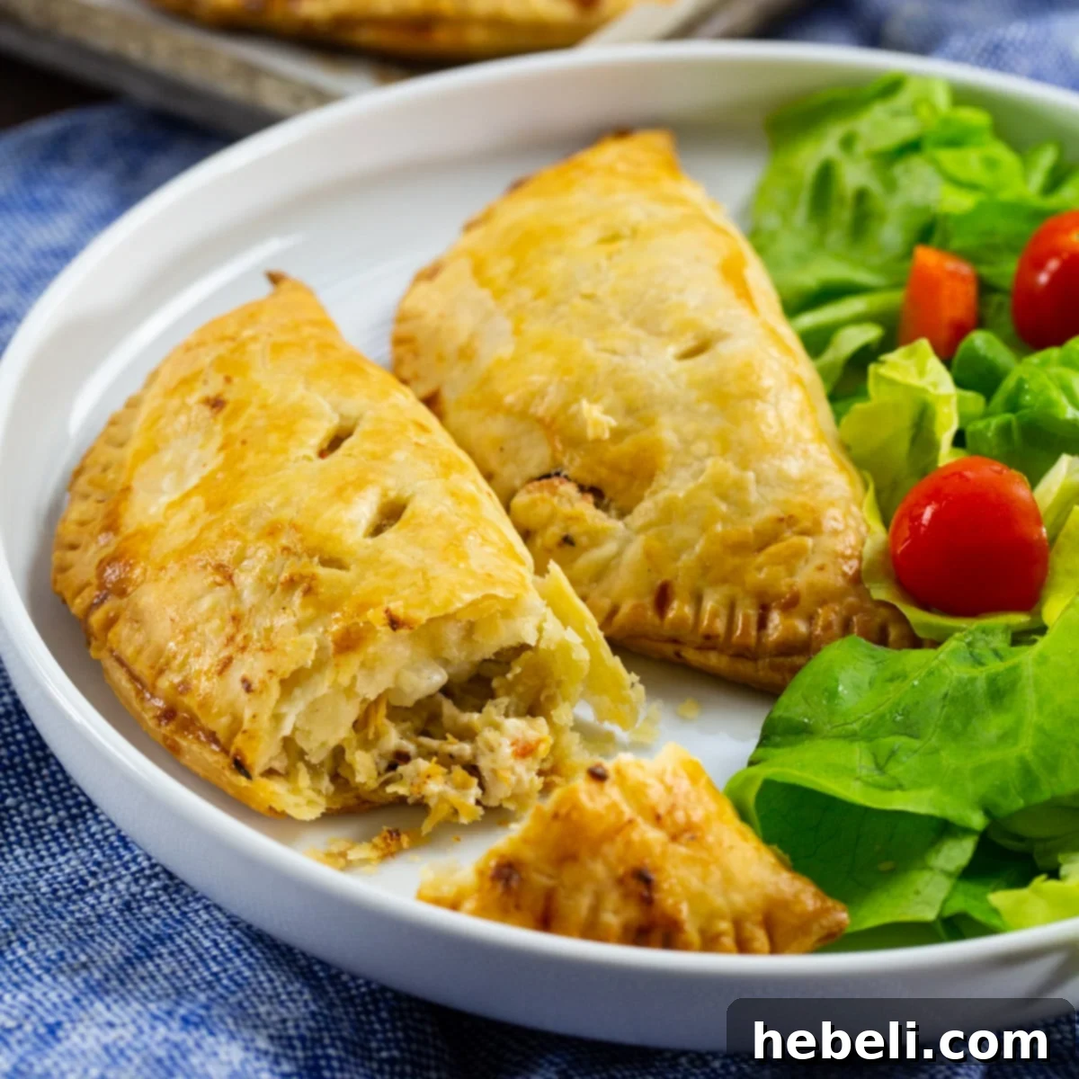 Creamy Chicken Pockets 2 Two golden-brown Creamy Chicken Hand Pies arranged neatly on a plate, accompanied by a fresh green salad, highlighting their versatility as a meal.