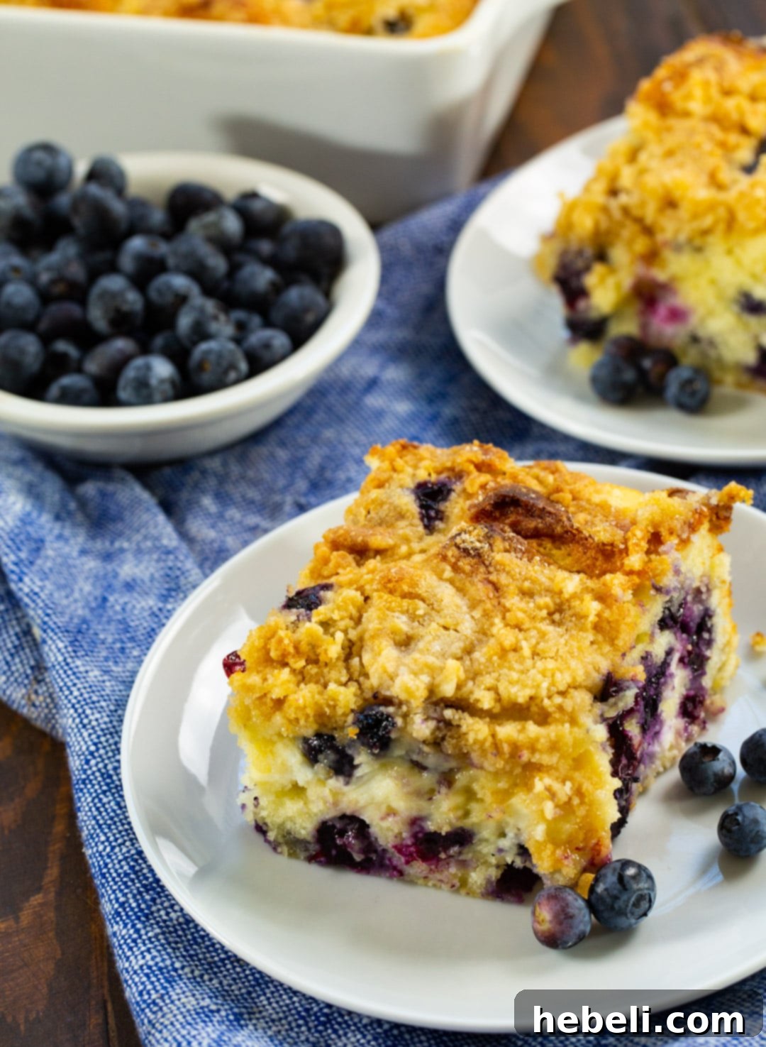 Decadent Blueberry Cream Cheese Coffee Cake 3 Two Slices of Blueberry Cream Cheese Coffee Cake on small plates, garnished with fresh blueberries.