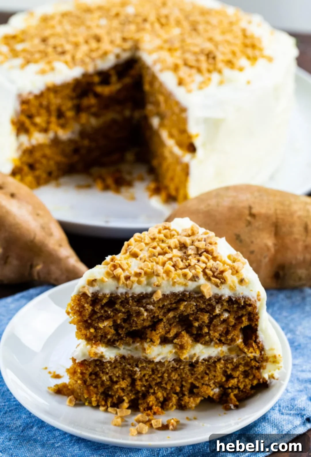 Velvet Sweet Potato Cake 4 A delectable slice of Sweet Potato Cake topped with generous cream cheese frosting and sprinkled with toffee bits on a plate, ready to be enjoyed.