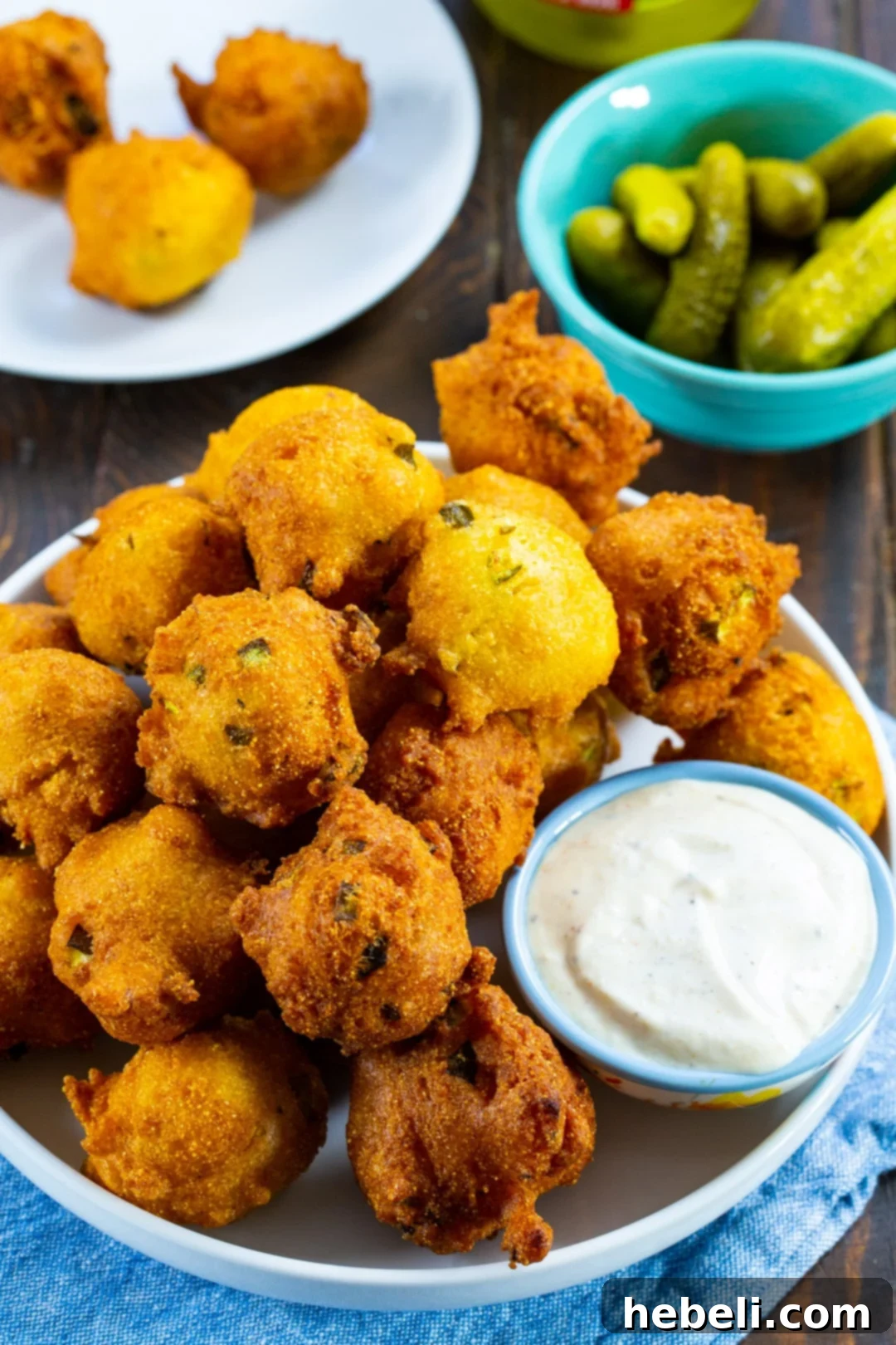 Piquant Pickle Hush Puppies 3 A rustic plate laden with crispy hush puppies and a side bowl brimming with crunchy dill pickle slices, showcasing the ingredients and the finished dish.