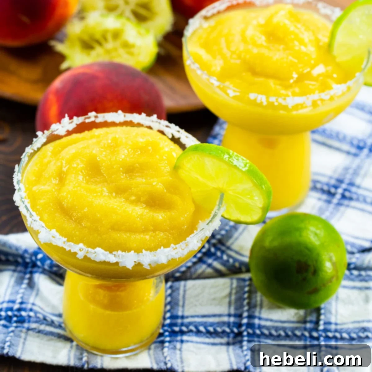 Frozen Peach Margaritas in elegant margarita glasses with salt around the rims, ready to be enjoyed.