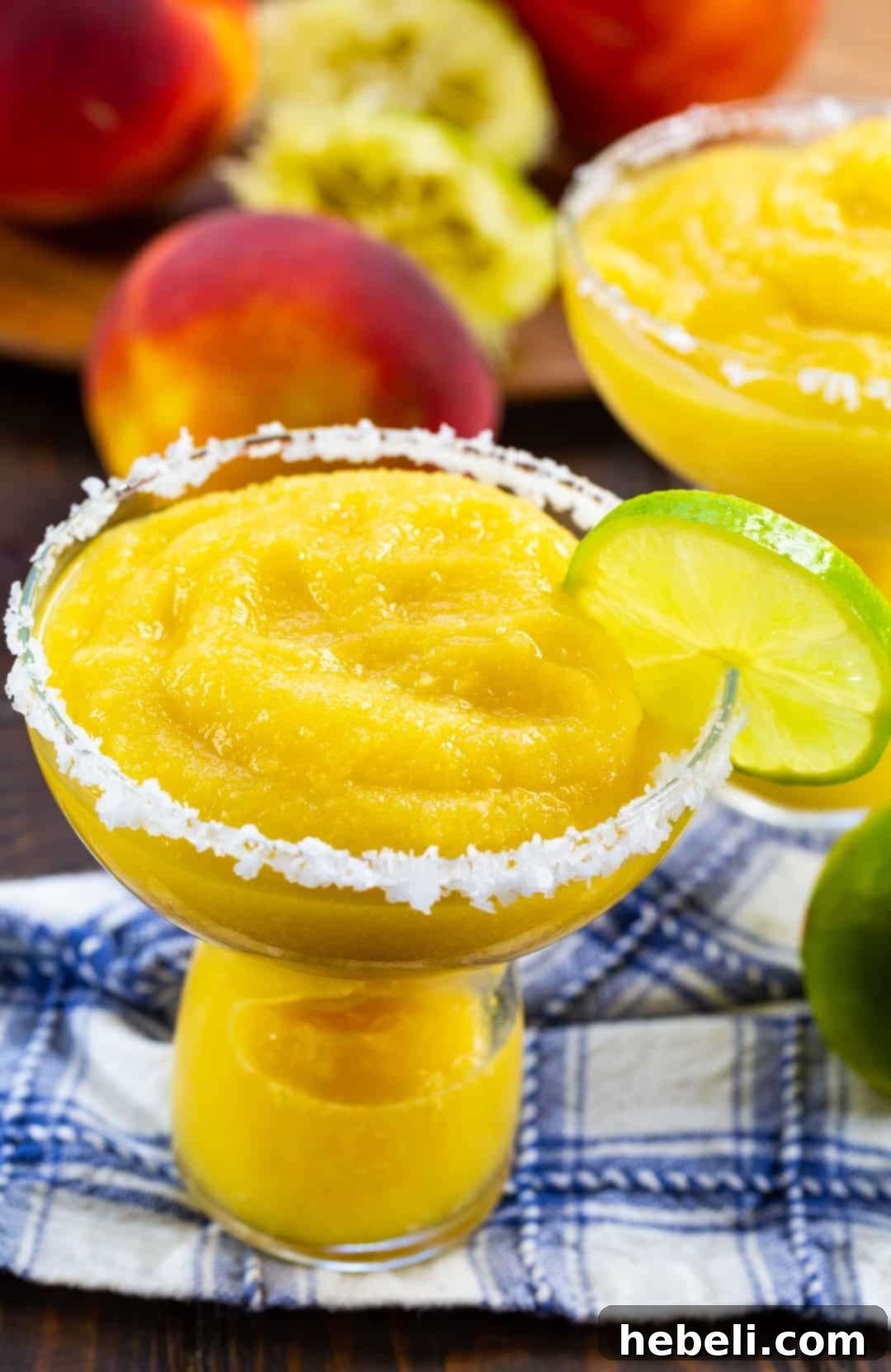Close-up of a single Frozen Peach Margarita glass, garnished with a lime slice and a salted rim, showcasing its vibrant color and frosty texture.