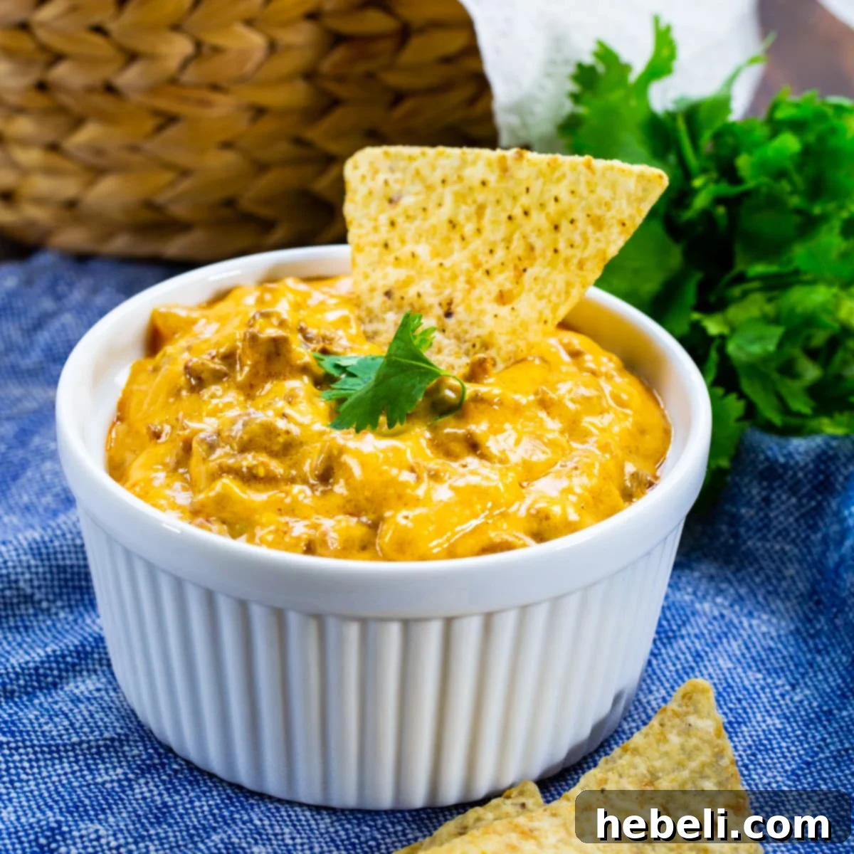 Your New Favorite 4-Ingredient Beef Enchilada Dip 2 A vibrant 4-Ingredient Beef Enchilada Dip served in a white bowl, with a crispy tortilla chip perfectly dipped into its creamy, cheesy goodness. The rich color of the dip hints at its savory flavor.