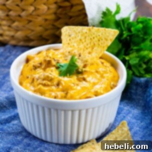 A top-down view of the 4-Ingredient Beef Enchilada Dip in a white slow cooker, showcasing its rich texture and inviting appearance. A portion of the dip is scooped out, ready for serving.