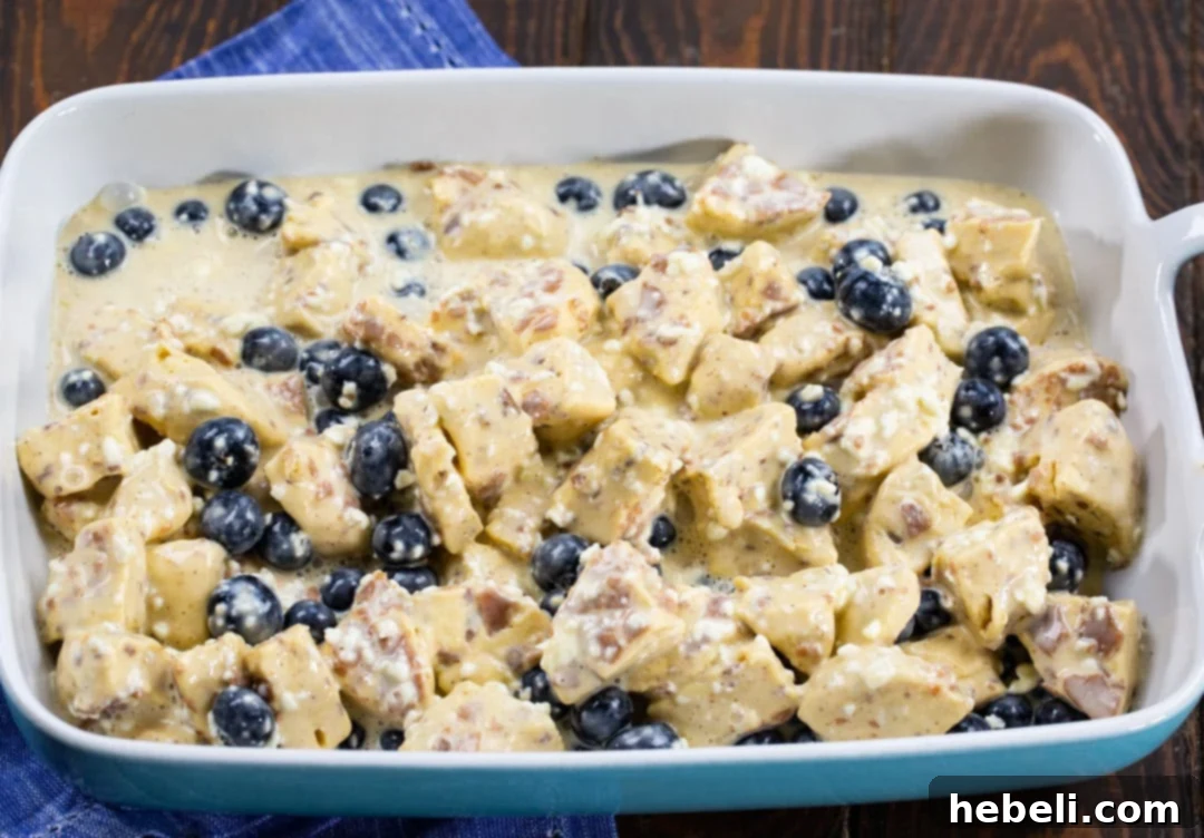 Unbaked blueberry cinnamon roll casserole mixture in a baking dish, ready for the oven.