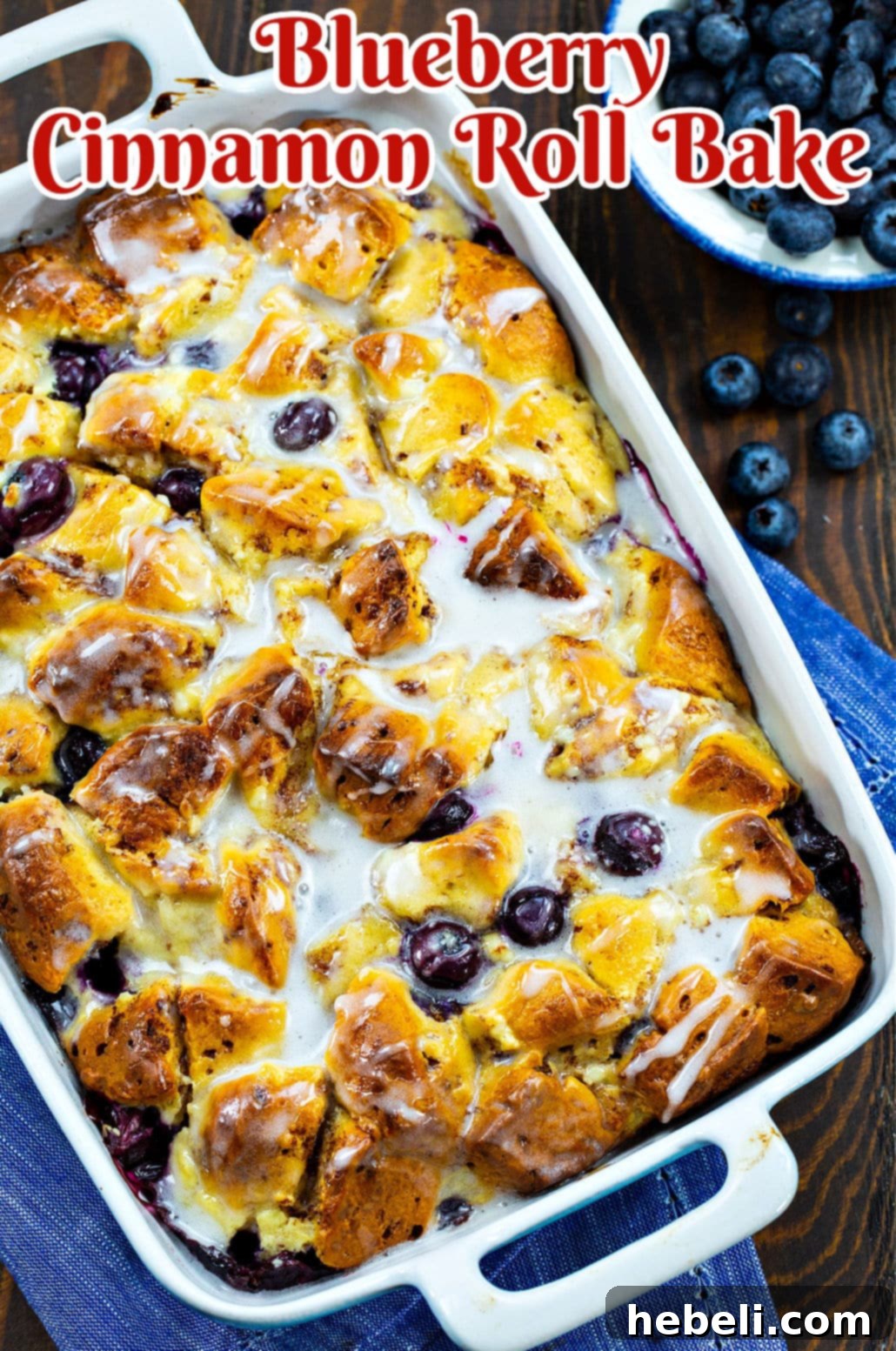 A close-up of the finished Blueberry Cinnamon Roll Bake in a baking dish, glistening with icing.