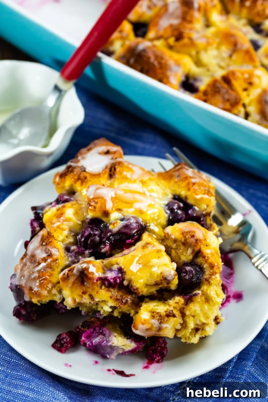 A slice of Blueberry Cinnamon Roll Bake dished up on a white plate, showing the layers of rolls and blueberries.