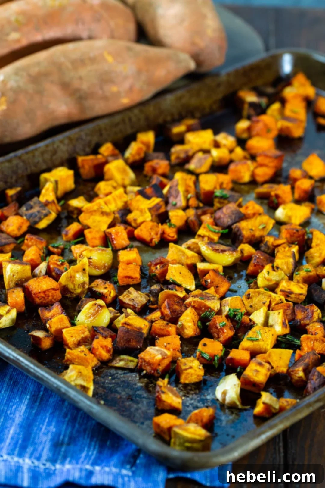Aromatic Rosemary Garlic Roasted Sweet Potatoes 3 Close-up of roasted sweet potatoes with herbs and garlic on a baking sheet, ready to be served.