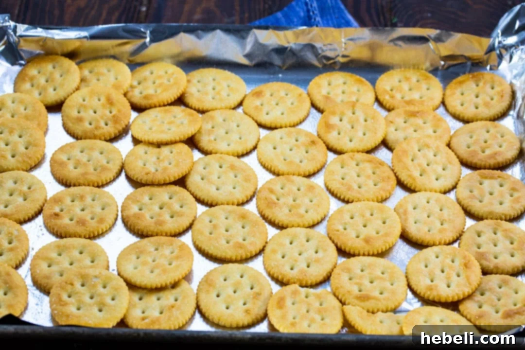 Crispy Ritz crackers meticulously arranged in a single, unbroken layer on a parchment-lined baking sheet, poised to receive the warm, golden toffee mixture.