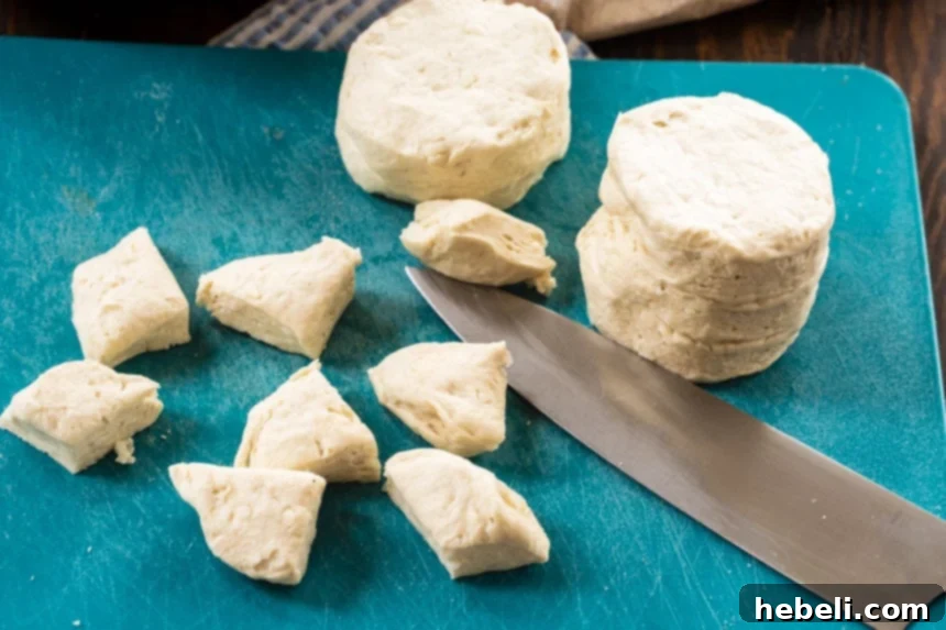 Refrigerated biscuit dough being cut into quarter-sized pieces on a cutting board, a crucial step for the pull-apart texture.