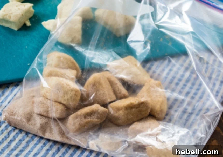 Biscuit pieces perfectly coated in cinnamon-sugar mixture inside a large plastic ziptop bag, ready to be transferred to the bundt pan.