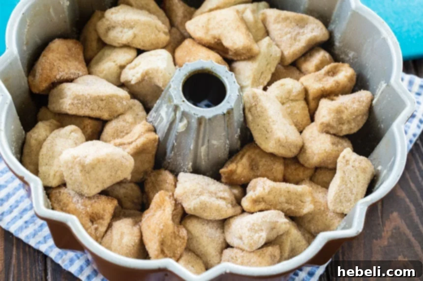Unbaked Monkey Bread mixture, featuring coated biscuit pieces and scattered pecans, artfully layered in a greased bundt pan before baking.