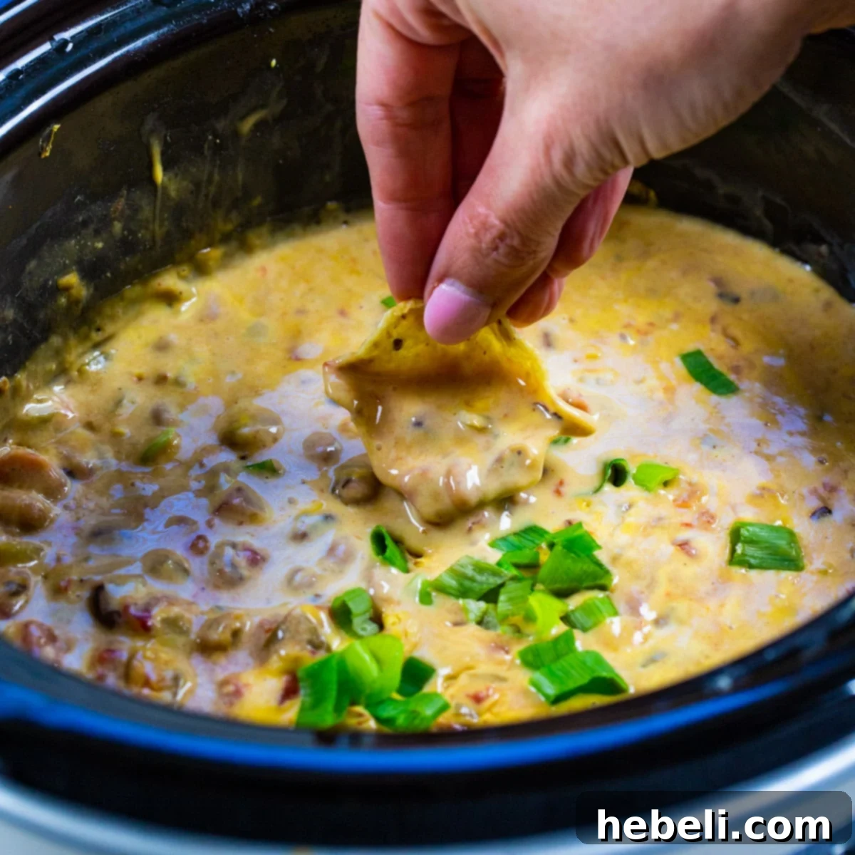 Hand dipping chip into a delicious Slow Cooker Black-Eyed Pea Dip.