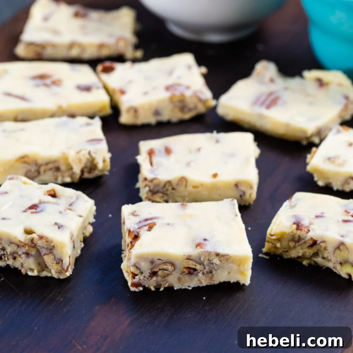 Squares of White Chocolate Pecan Candy artfully arranged on a rustic wooden board, showcasing their golden-brown pecan pieces.