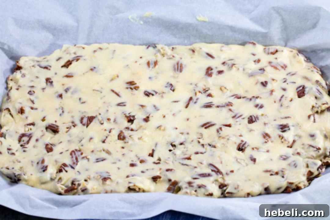 Uncut slab of White Chocolate Pecan Candy cooling in a jelly roll pan lined with parchment paper, revealing a dense mixture of pecans.