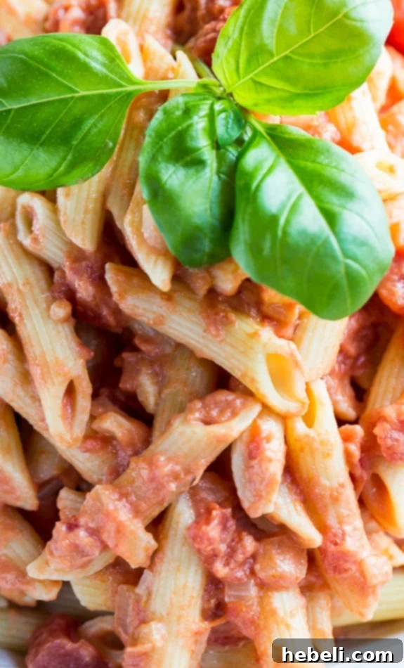 Close-up shot of Penne Alla Vodka in a white bowl, showcasing the creamy sauce clinging to the pasta, with fresh basil leaves as a garnish.