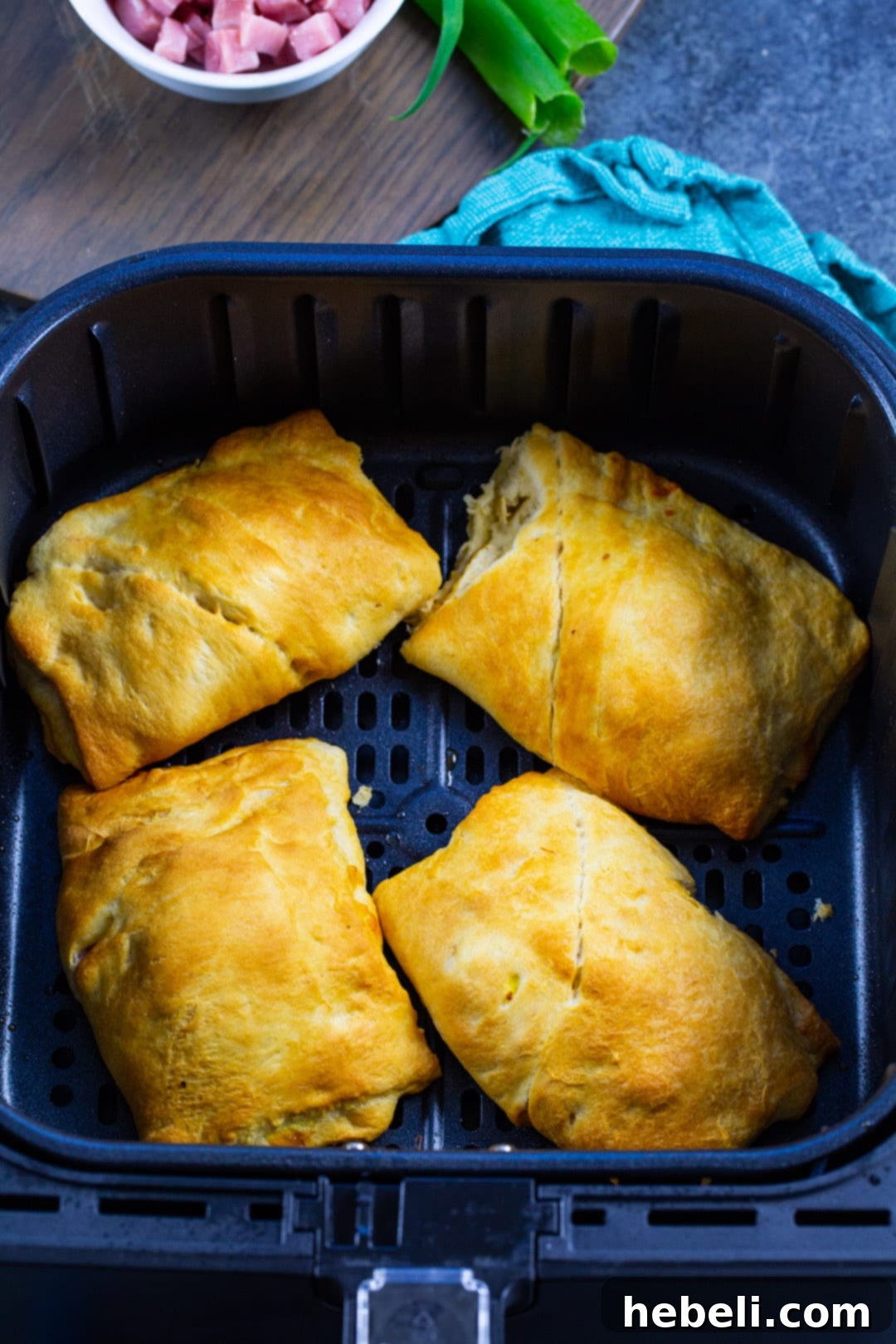 Air Fryer Ham and Egg Bundles 3 Ham and Egg Pockets cooking in an air fryer basket, achieving a perfect golden-brown.